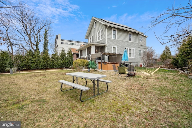 rear view of property featuring a lawn and a hot tub