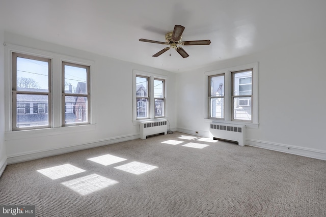 carpeted empty room featuring a ceiling fan, baseboards, and radiator heating unit