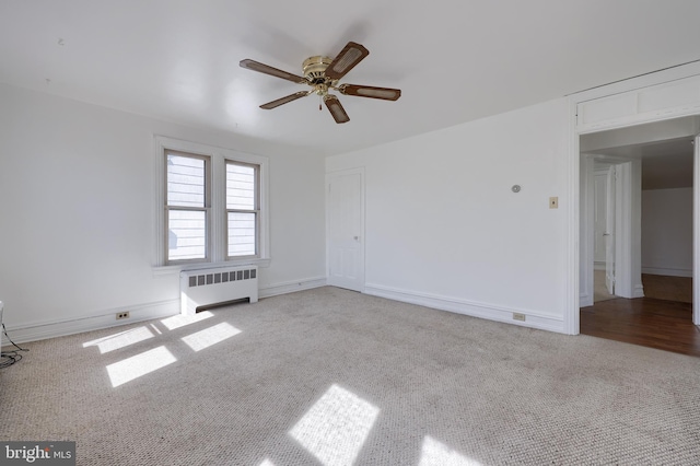 carpeted empty room with radiator heating unit, baseboards, and ceiling fan