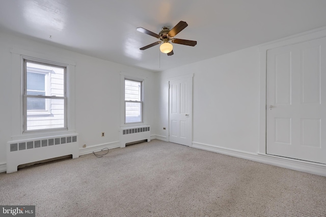 carpeted empty room with baseboards, ceiling fan, and radiator