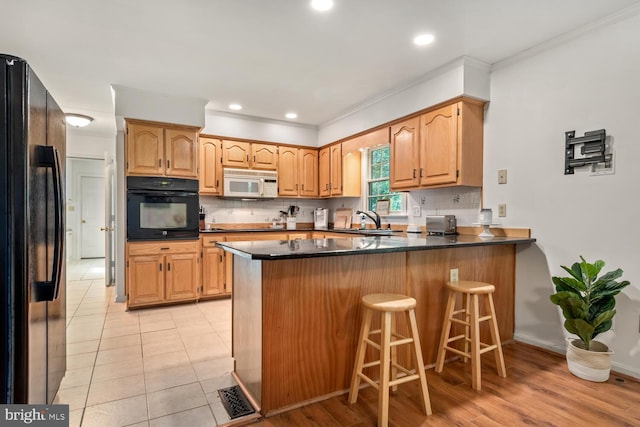 kitchen featuring a kitchen breakfast bar, backsplash, a peninsula, black appliances, and a sink