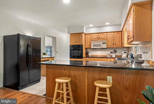 kitchen featuring decorative backsplash, a sink, dark stone countertops, a peninsula, and black appliances