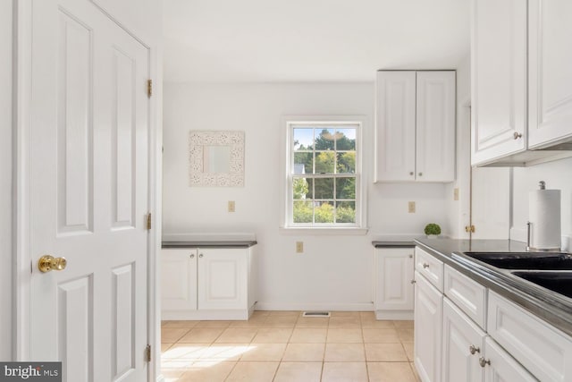 kitchen with light tile patterned floors, dark countertops, white cabinetry, and baseboards