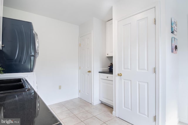 clothes washing area with stacked washer and dryer, light tile patterned floors, and cabinet space