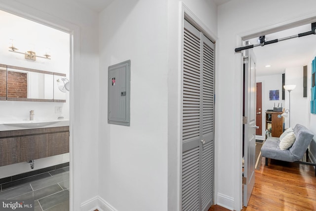 corridor with electric panel, a sink, baseboards, and wood finished floors