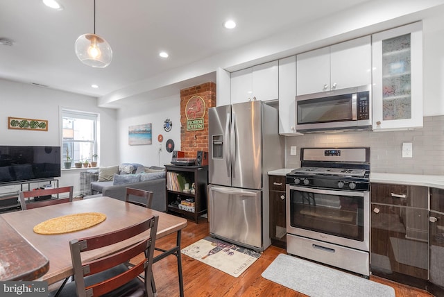 kitchen with white cabinets, light wood finished floors, stainless steel appliances, and backsplash