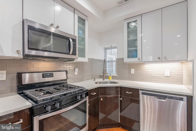 kitchen with a sink, white cabinets, light countertops, appliances with stainless steel finishes, and dark brown cabinets