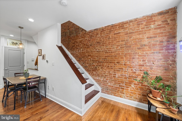 staircase featuring brick wall, baseboards, and wood finished floors