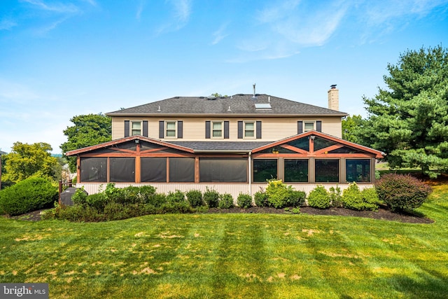 rear view of house featuring a sunroom, a shingled roof, a chimney, and a yard