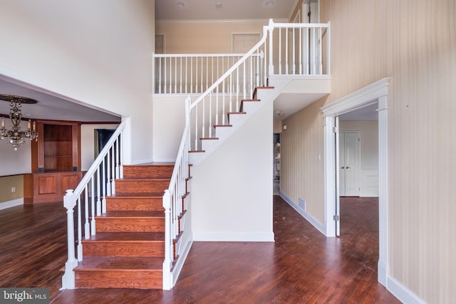 staircase featuring baseboards, a high ceiling, wood finished floors, and an inviting chandelier