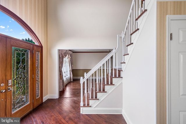 foyer with a towering ceiling, baseboards, and wood finished floors