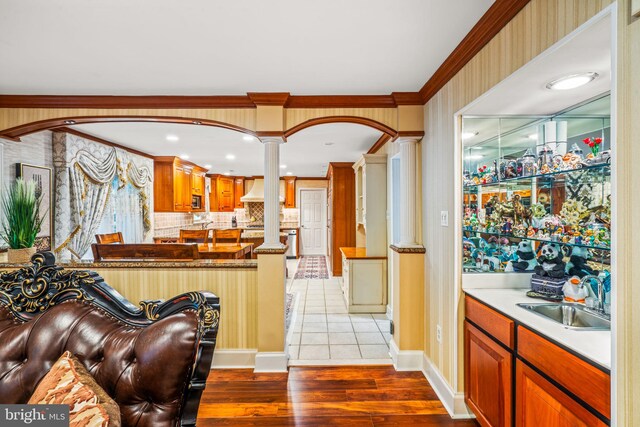 kitchen featuring wood finished floors, a sink, ornamental molding, custom exhaust hood, and ornate columns