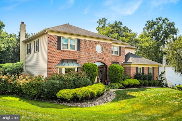 view of front of home with brick siding, a chimney, and a front yard