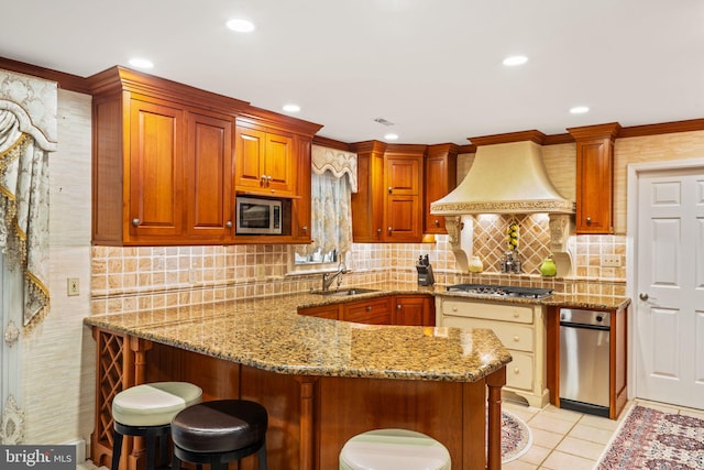 kitchen with light tile patterned floors, appliances with stainless steel finishes, light stone countertops, premium range hood, and a sink