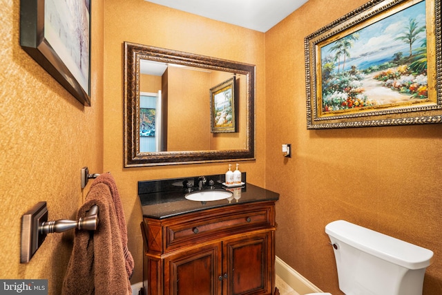 half bath featuring baseboards, vanity, and toilet