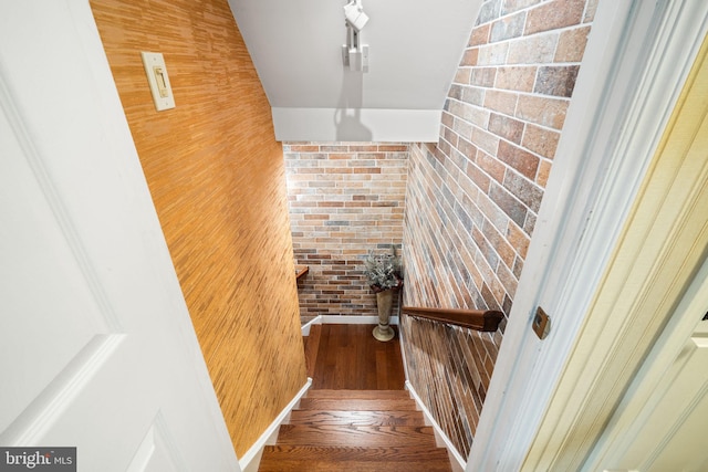 stairway with brick wall and wood finished floors