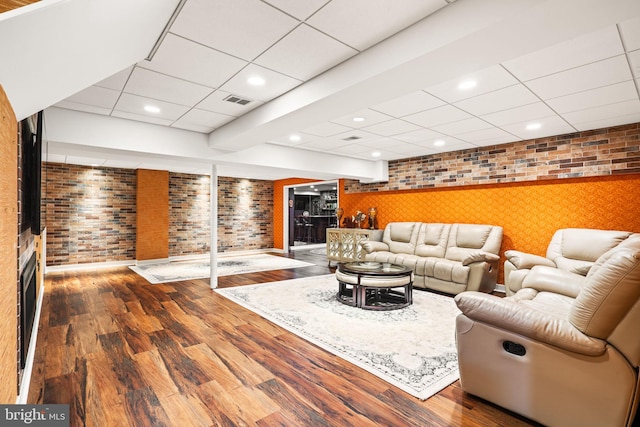 living room with brick wall, a drop ceiling, wood finished floors, and visible vents