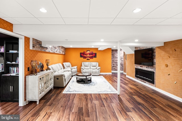 living area with a drop ceiling, a fireplace, wood finished floors, baseboards, and wallpapered walls