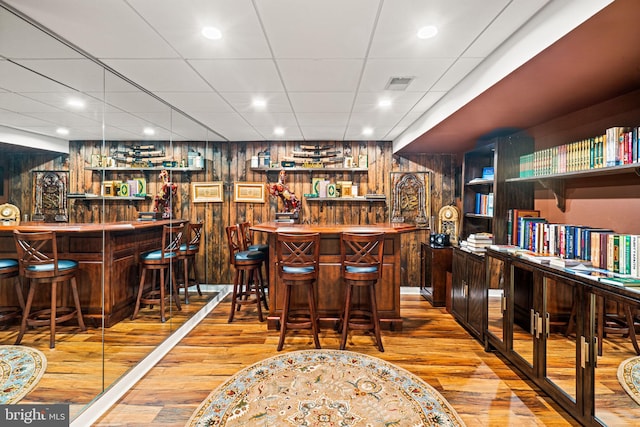 bar with wooden walls, visible vents, bar, wood finished floors, and a paneled ceiling