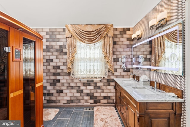 bathroom featuring brick wall, double vanity, and a sink