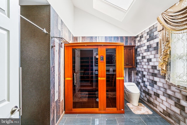 bathroom with vaulted ceiling with skylight, a shower, brick wall, and toilet