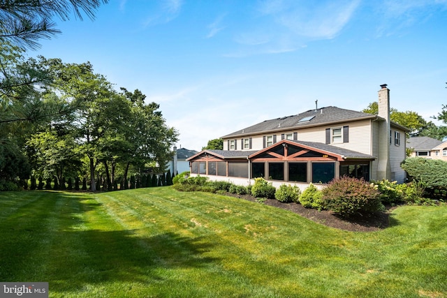 back of property featuring a sunroom, a yard, and a chimney