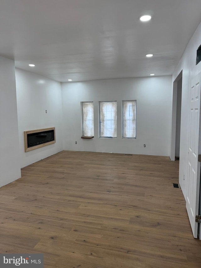 unfurnished living room featuring recessed lighting, visible vents, wood finished floors, and a glass covered fireplace