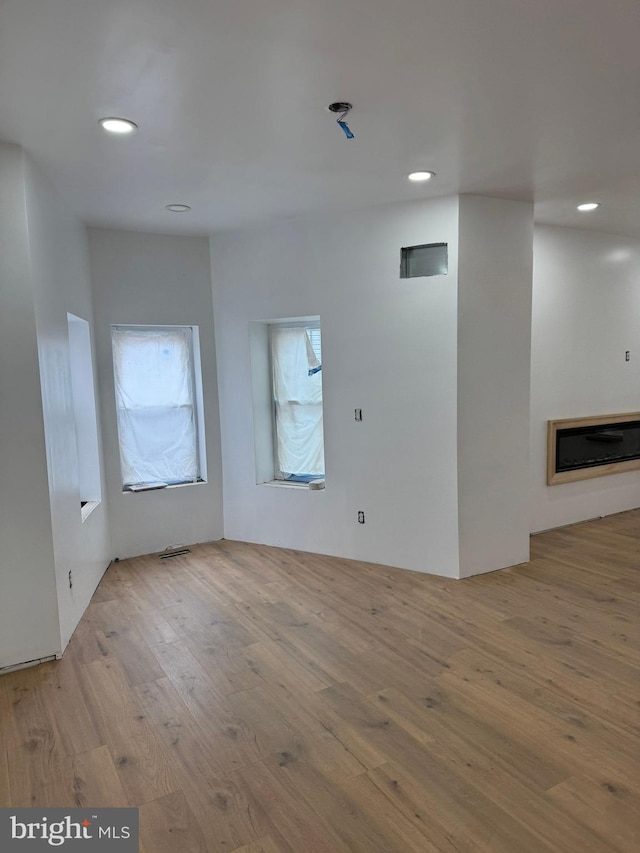 interior space featuring visible vents, a glass covered fireplace, wood finished floors, and recessed lighting