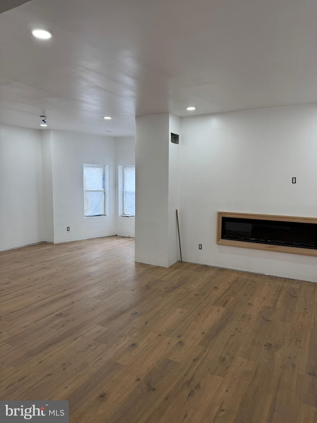 spare room featuring recessed lighting, wood-type flooring, and a glass covered fireplace