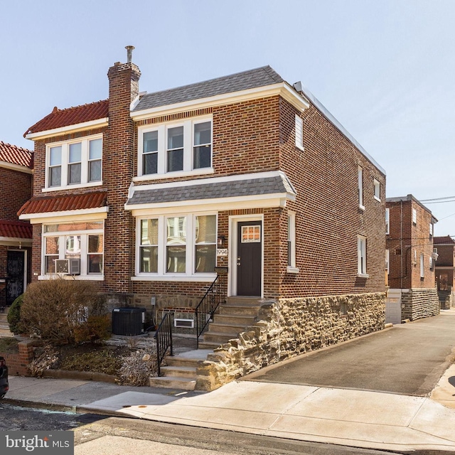 view of front of home with brick siding, central AC unit, a chimney, and a shingled roof