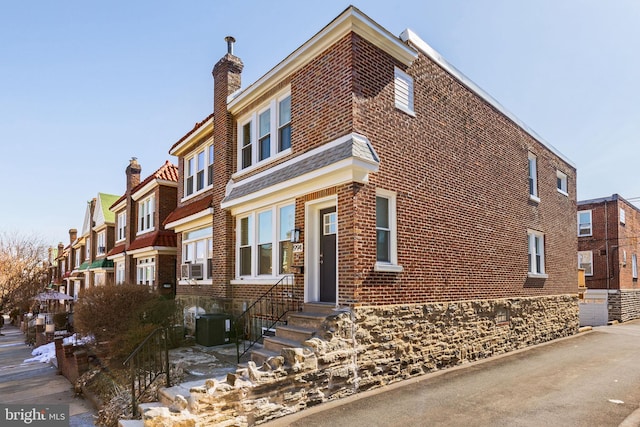 view of front facade with central AC unit, a residential view, a chimney, entry steps, and brick siding