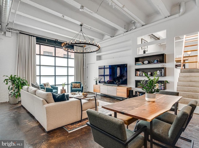 living area featuring concrete floors, beam ceiling, a notable chandelier, and stairway