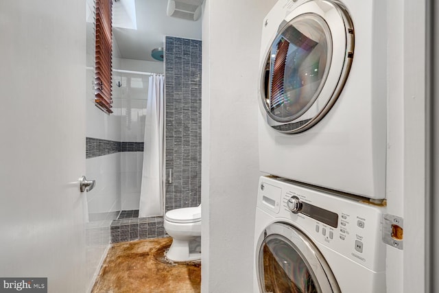 interior space featuring toilet, stacked washing maching and dryer, and a tile shower