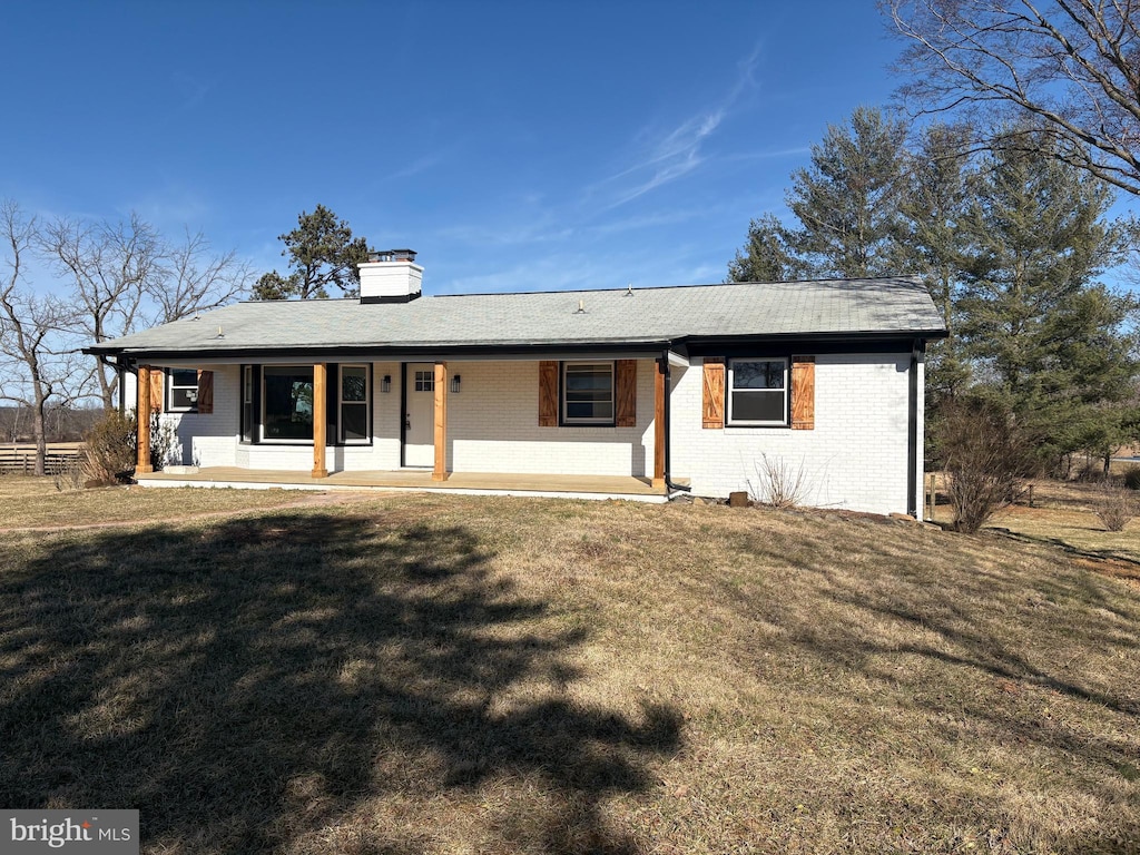 back of property with brick siding, a porch, a chimney, and a yard