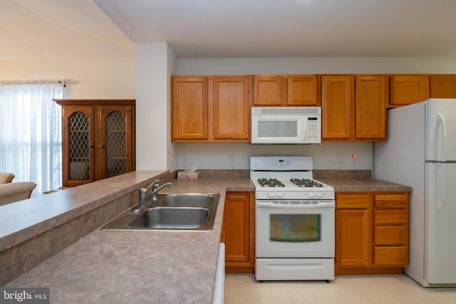 kitchen with a peninsula, white appliances, brown cabinetry, and a sink