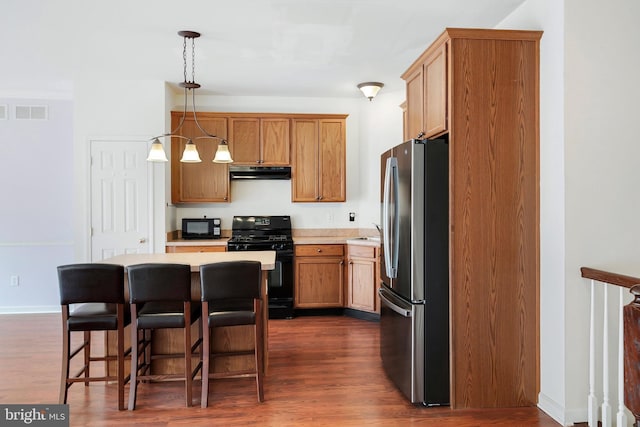 kitchen featuring dark wood-type flooring, under cabinet range hood, light countertops, a kitchen breakfast bar, and black appliances