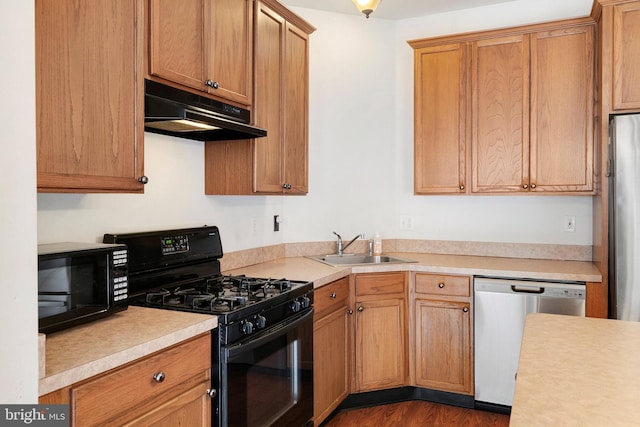 kitchen with under cabinet range hood, light countertops, dark wood-style floors, black appliances, and a sink