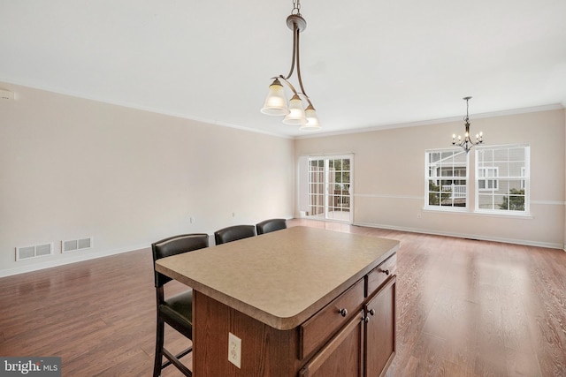 kitchen with decorative light fixtures, visible vents, a center island, and wood finished floors