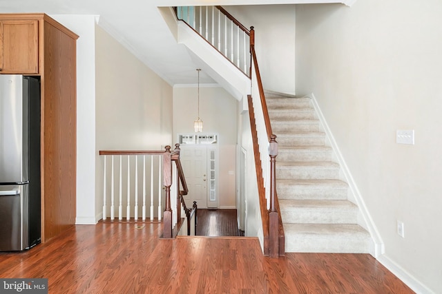 stairs with baseboards, crown molding, a towering ceiling, and wood finished floors