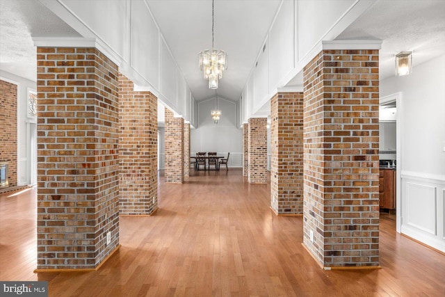 corridor with a decorative wall, an inviting chandelier, wainscoting, a textured ceiling, and hardwood / wood-style floors