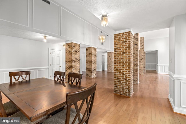 dining area with a decorative wall, a textured ceiling, light wood finished floors, and decorative columns