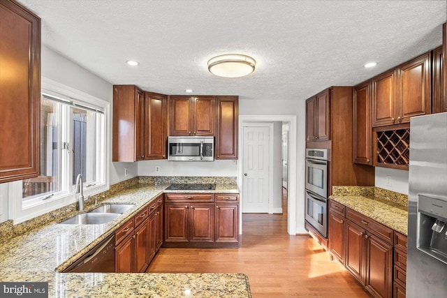 kitchen featuring a textured ceiling, a sink, light wood-type flooring, light stone countertops, and black appliances