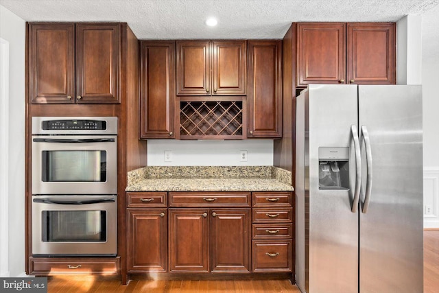 kitchen featuring a textured ceiling, appliances with stainless steel finishes, light stone counters, and wood finished floors