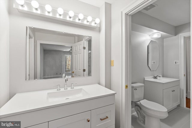 bathroom featuring toilet, visible vents, two vanities, and a sink