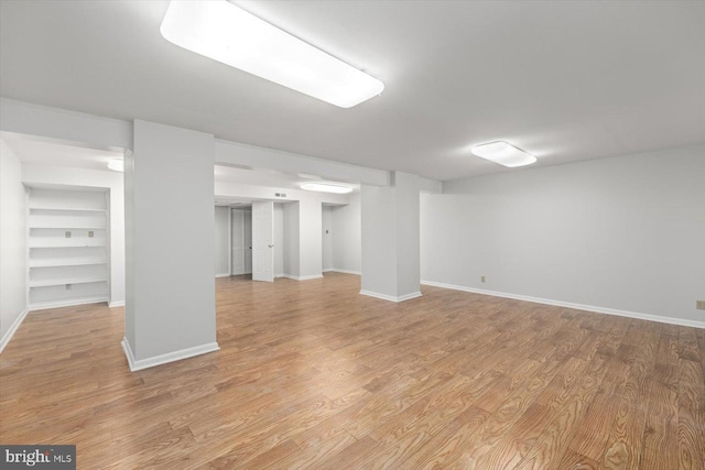 finished below grade area with built in features, light wood-type flooring, and baseboards