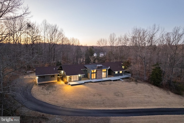 view of front facade with a deck, dirt driveway, and a view of trees