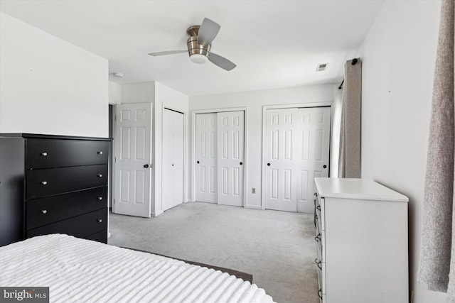 bedroom featuring a ceiling fan, two closets, visible vents, and light colored carpet