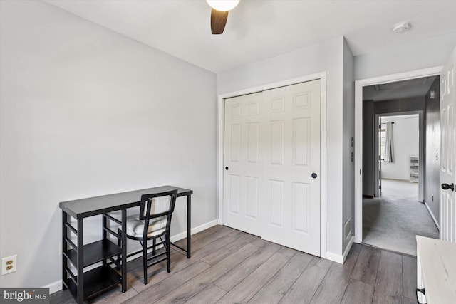 home office with attic access, a ceiling fan, baseboards, and wood finished floors