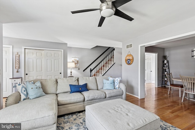 living area featuring wood finished floors, visible vents, baseboards, stairs, and a ceiling fan