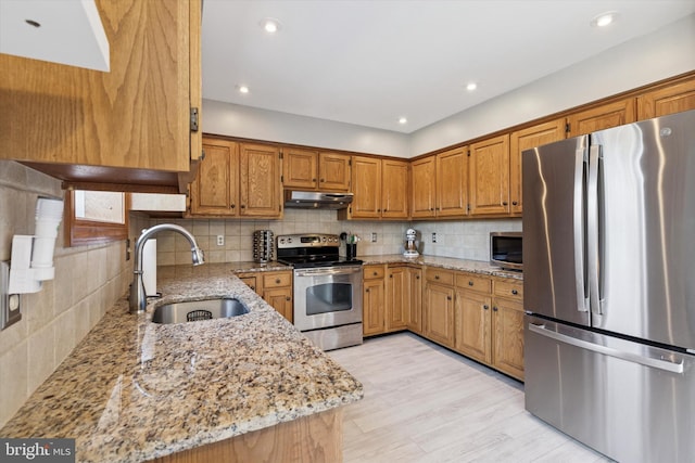 kitchen with tasteful backsplash, appliances with stainless steel finishes, light stone countertops, under cabinet range hood, and a sink